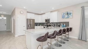 Cocina moderna con armarios blancos, una isla central con taburetes de bar, un refrigerador de acero inoxidable y un microondas.
