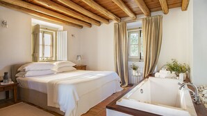 Un dormitorio con una cama grande, techo de madera, baño con bañera y ventana con cortinas.