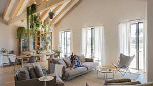 Amplio salón con techo alto, vigas de madera, sofá, mesa de comedor y una ventana grande con cortinas.