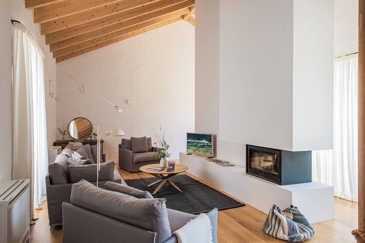Ein modernes Wohnzimmer mit Kamin, grauen Sofas, einem Couchtisch und einem großen Fenster.