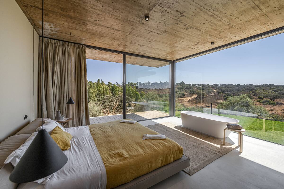 Ein modernes Schlafzimmer mit einem großen Bett, einer Badewanne und Blick auf die Landschaft.