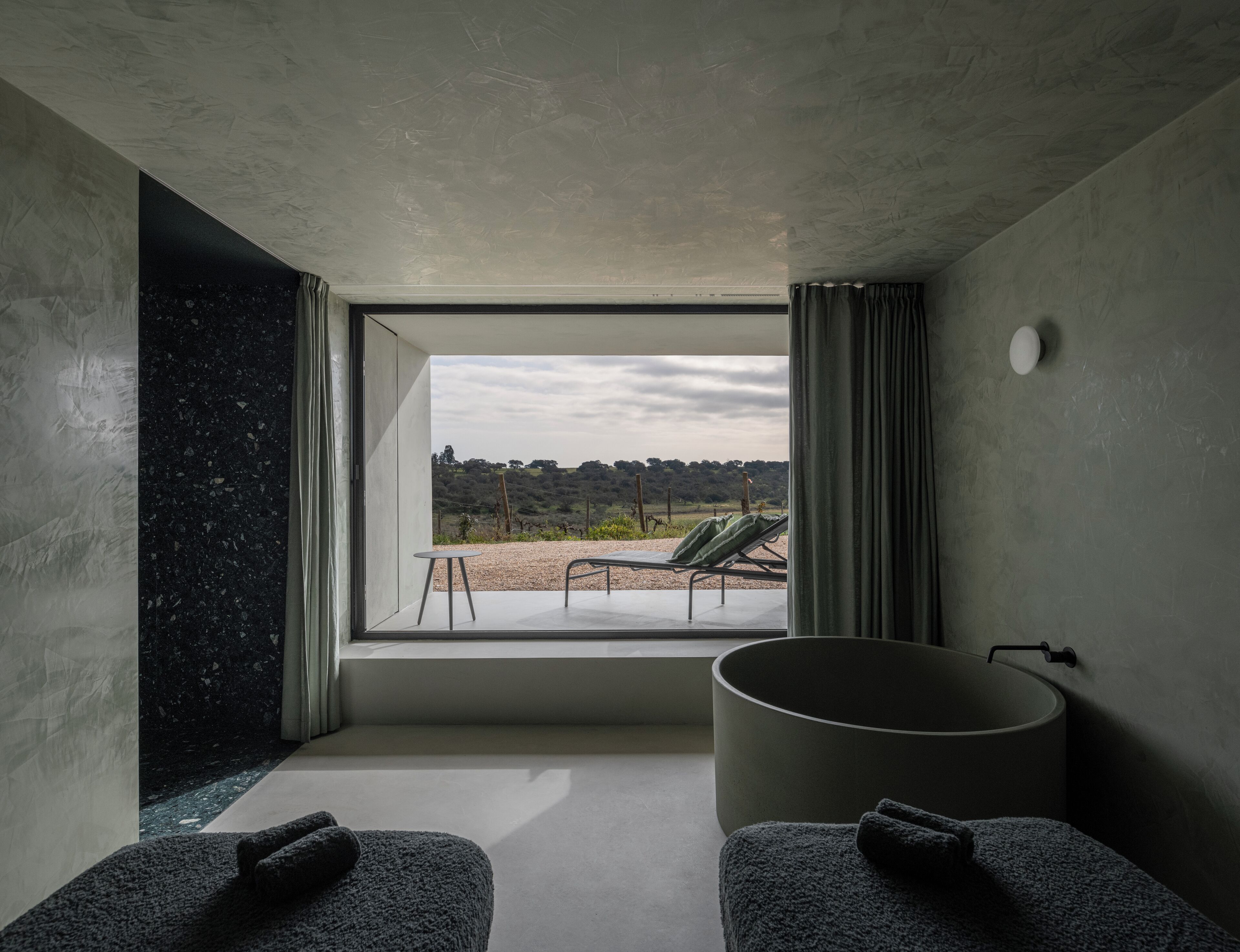 Un baño moderno con un ventanal grande, una bañera y dos toallas sobre un banco.