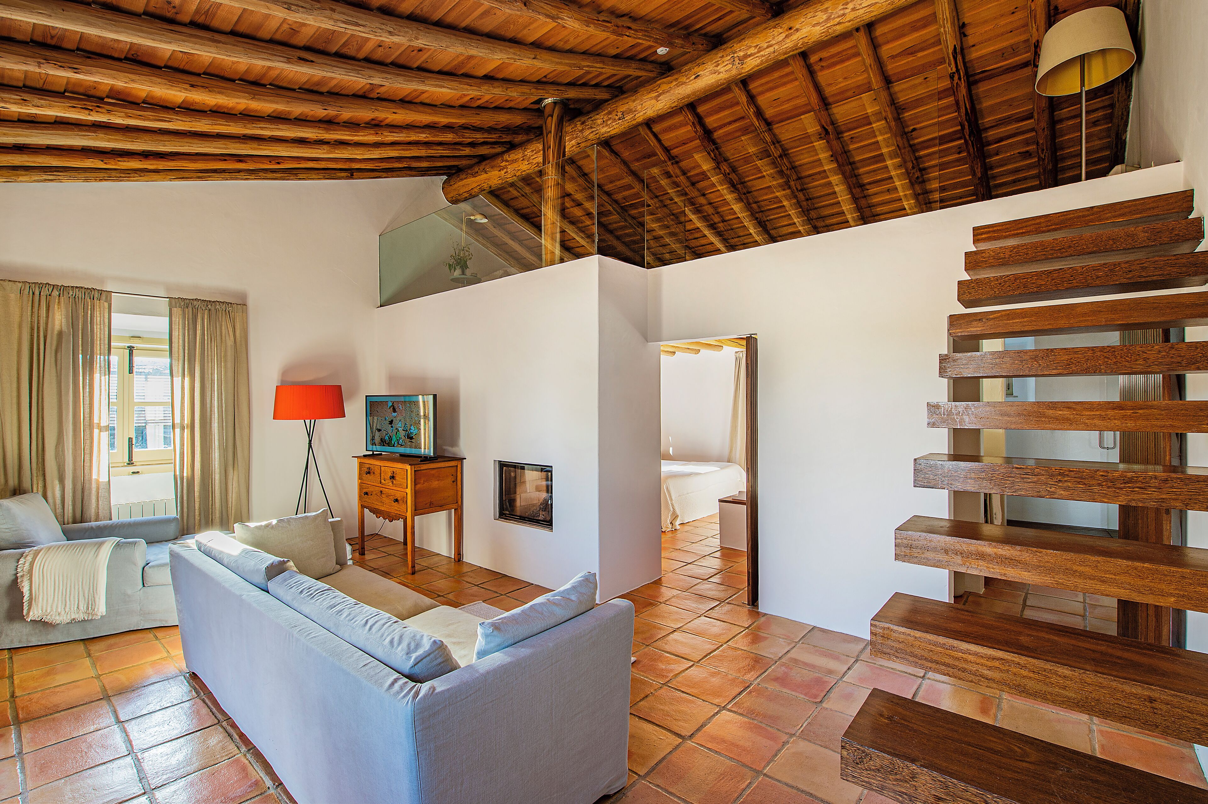 A spacious living area with a wooden staircase, a sofa, a lamp, and a view of the outside.