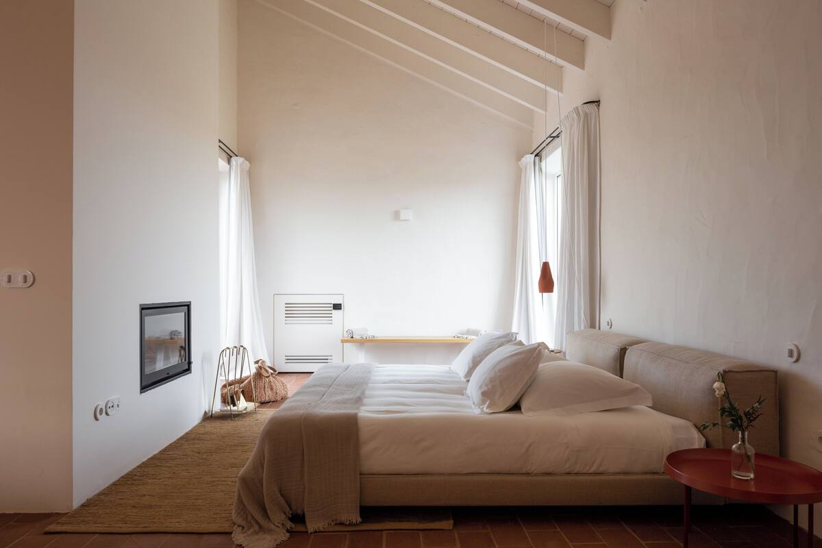 Ein Schlafzimmer mit Bett, Nachttisch, Stuhl, Heizkörper und einem Fenster mit Vorhängen.
