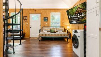 A bedroom with a bed, a washing machine, and a TV displaying 'Creekside Cabin Lake Hartwell'.