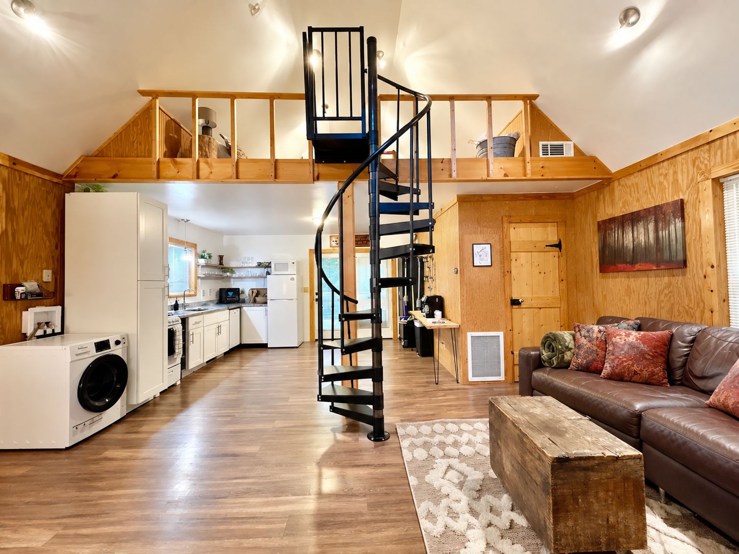 Un vaste espace de vie agrémenté d’un escalier central, une cuisine équipée d’appareils électroménagers modernes et un coin salon confortable avec un canapé en cuir.