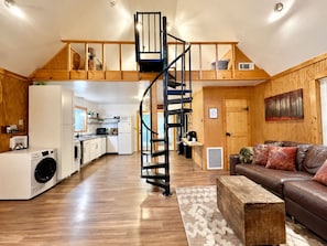 A spacious living area with a central staircase, a kitchen with modern appliances, and a cozy seating area with a leather sofa.