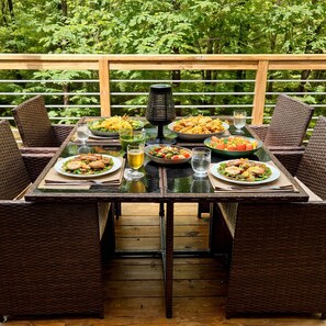 A dining table set outdoors with wicker chairs, surrounded by various dishes and drinks. - Romantic Cabin: Hot Tub, Fire Pit, Indoor & Outdoor Living, EV Charger (Martin)