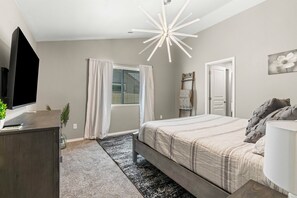 Relax in a serene bedroom with a large bed, flat-screen TV, and unique ceiling light fixture.