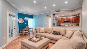 Una sala de estar amplia con un sofá seccional en forma de L, un comedor con una mesa redonda y sillas, y una cocina con armarios de madera y un microondas.