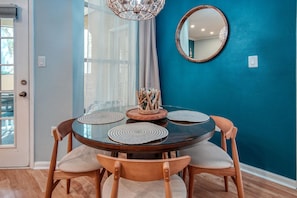 Un coin repas avec une table ronde en verre, des chaises en bois et un miroir sur un mur de couleur turquoise.