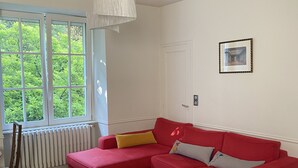 A modern living room with a red sectional sofa, a grey coffee table, and a large window with a view of greenery.