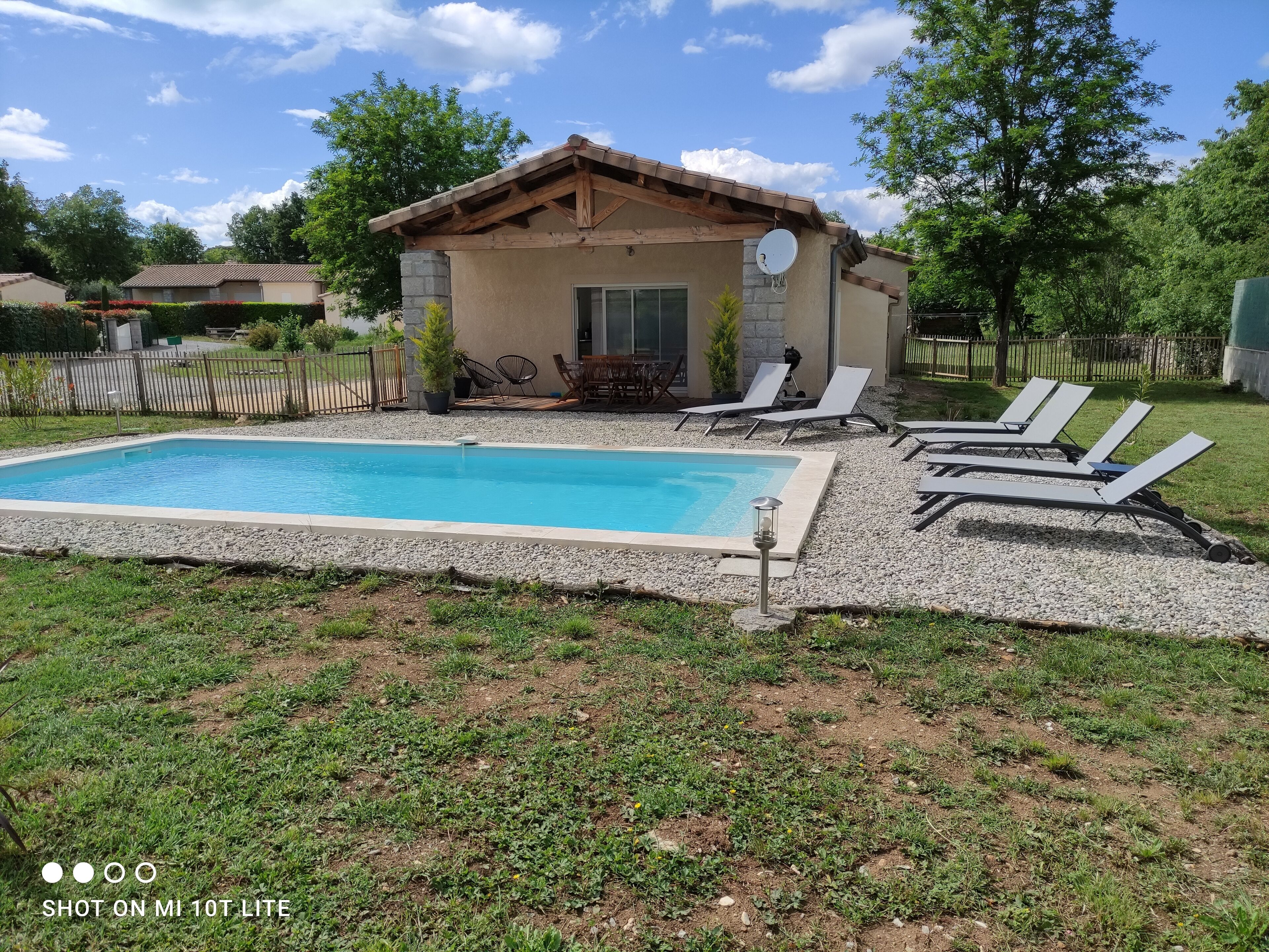 A swimming pool with lounge chairs, a small building with a satellite dish, and a fenced yard.