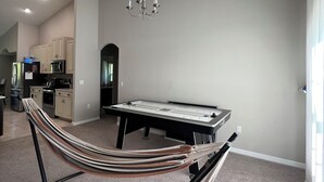 Un salon moderne avec une table de billard, un hamac et un coin cuisine à l’arrière-plan.