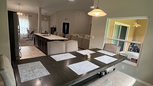Une salle à manger moderne avec une table en bois foncé, des chaises recouvertes d’un tissu beige et un lustre.