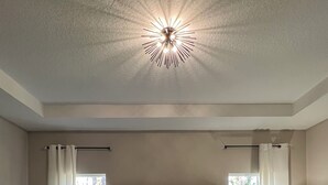 Une chambre à coucher avec une tête de lit capitonnée, un grand lit recouvert d’une courtepointe, deux tables de chevet avec des lampes et un luminaire au plafond.
