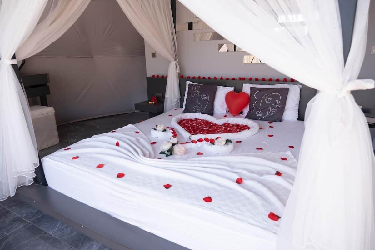 A bed with a canopy, white bedding, and red rose petals.