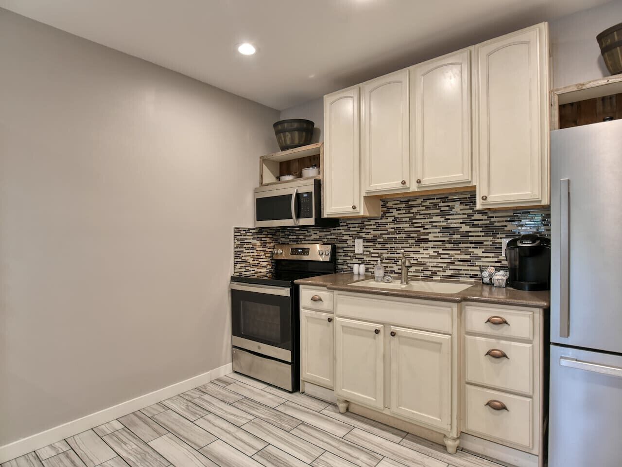 A compact kitchen with white cabinetry, a stainless steel refrigerator, a microwave, and a stove.