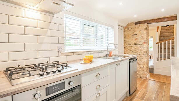 A modern kitchen with a gas stove, oven, white cabinets, a window with blinds, and a stone wall. - 2 bedroom accommodation in Snitterby (Snitterby)