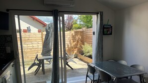 A room with a sliding glass door leading to a patio, a dining table with chairs, and a small kitchen area. - Landes house Dax (Dax)
