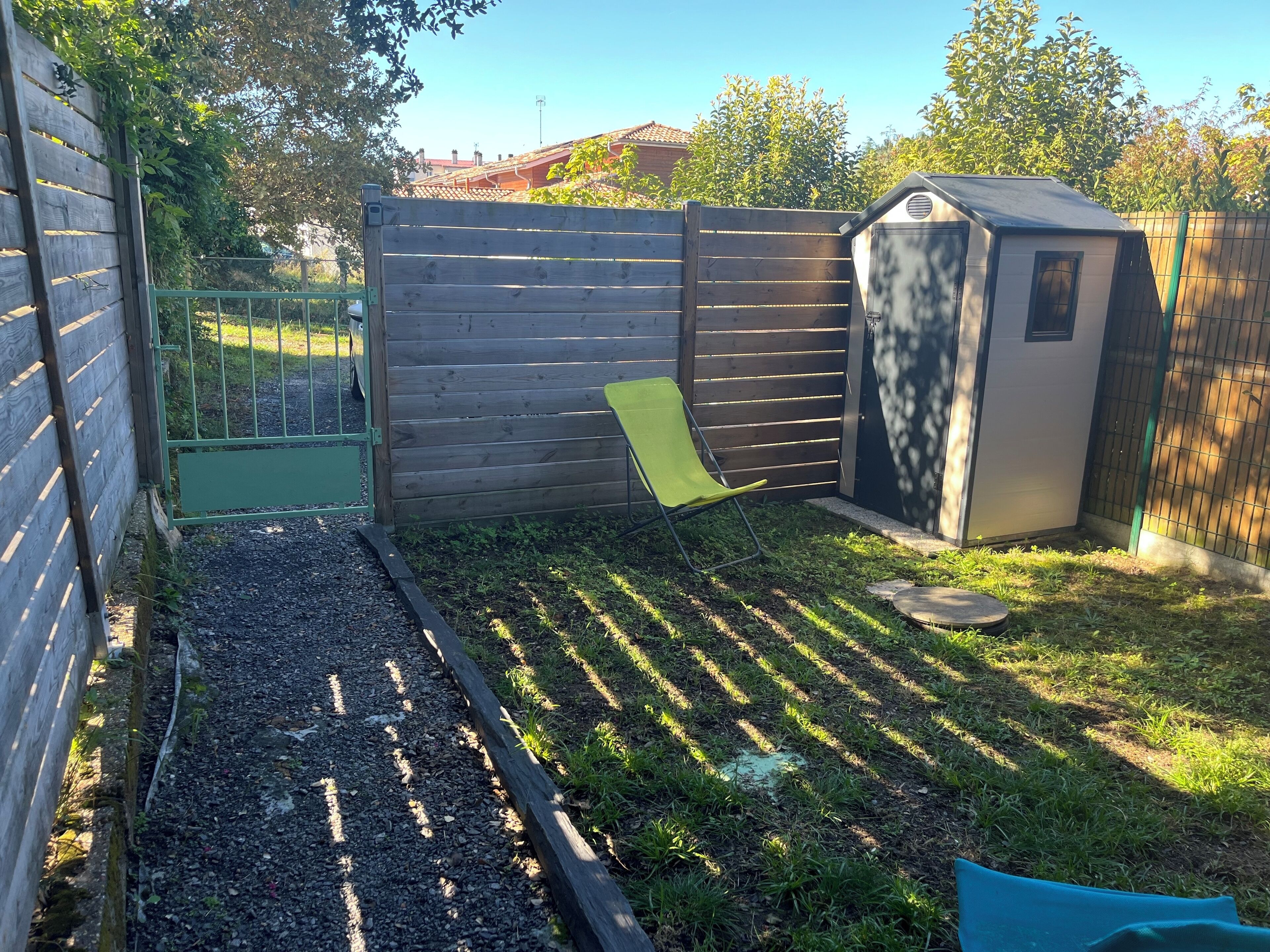 A backyard with a wooden fence, a green chair, a shed, and a garden bed with gravel.