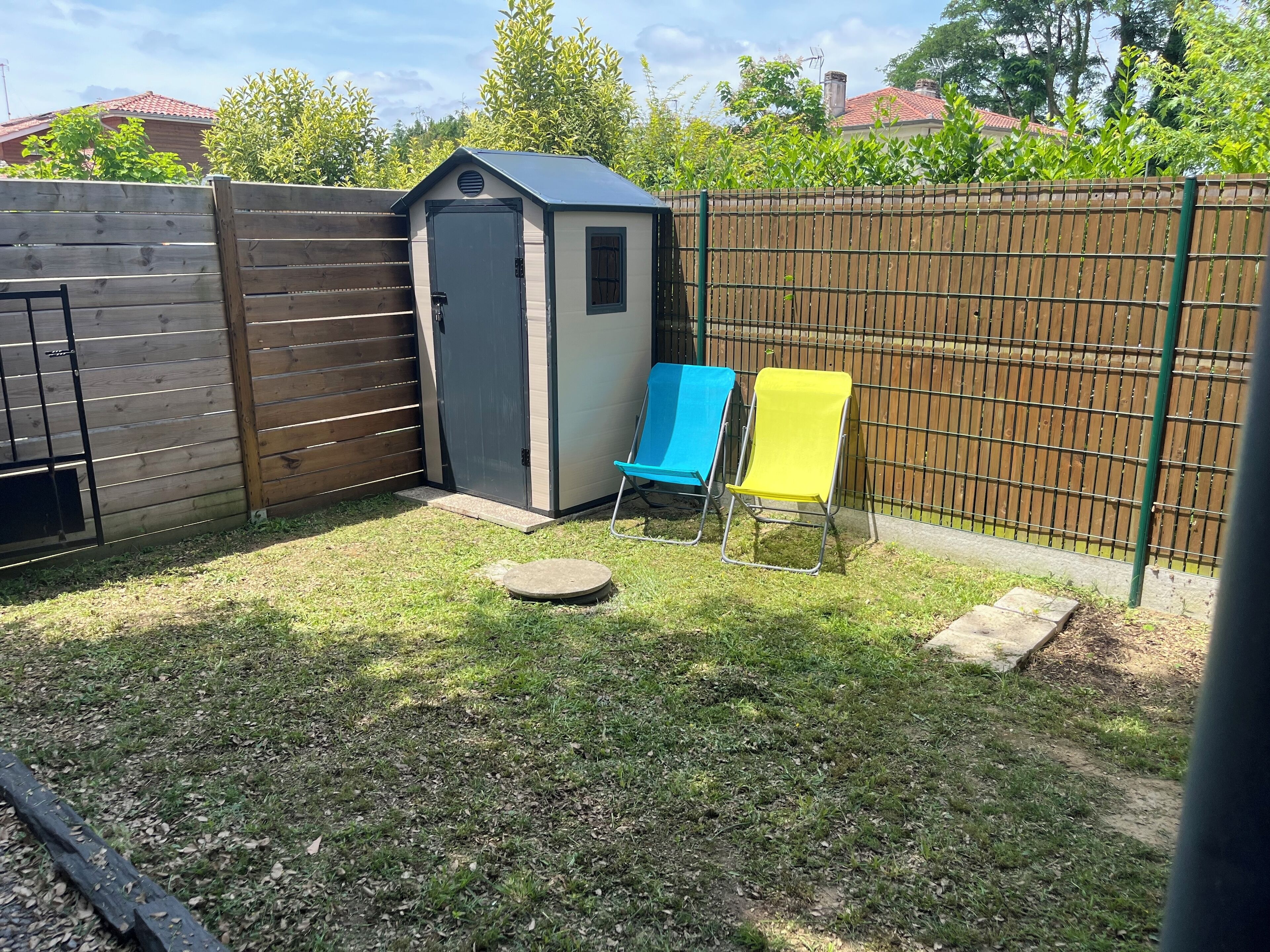 Een achtertuin met een houten omheining, een tuinhuisje en twee tuinstoelen.