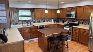 A modern kitchen with wooden cabinets, a central island with bar stools, stainless steel appliances, and pendant lighting. - Coldwater Lake Spacious Lake Drive Getaway (Coldwater)