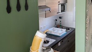 Et køkken med mikroovn, vask og træskabe. Der er sorte redskaber på væggen og en kaffemaskine på bordet.