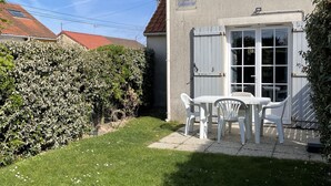 Et hus med røde tegltag, hvide facader og en lille patio med et bord og stole.