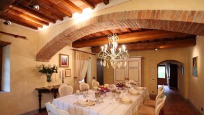 A dining room with a long table set for a meal, featuring a chandelier and rustic brick walls. - Villa Consolata, Large country villa with pool (Reggello)