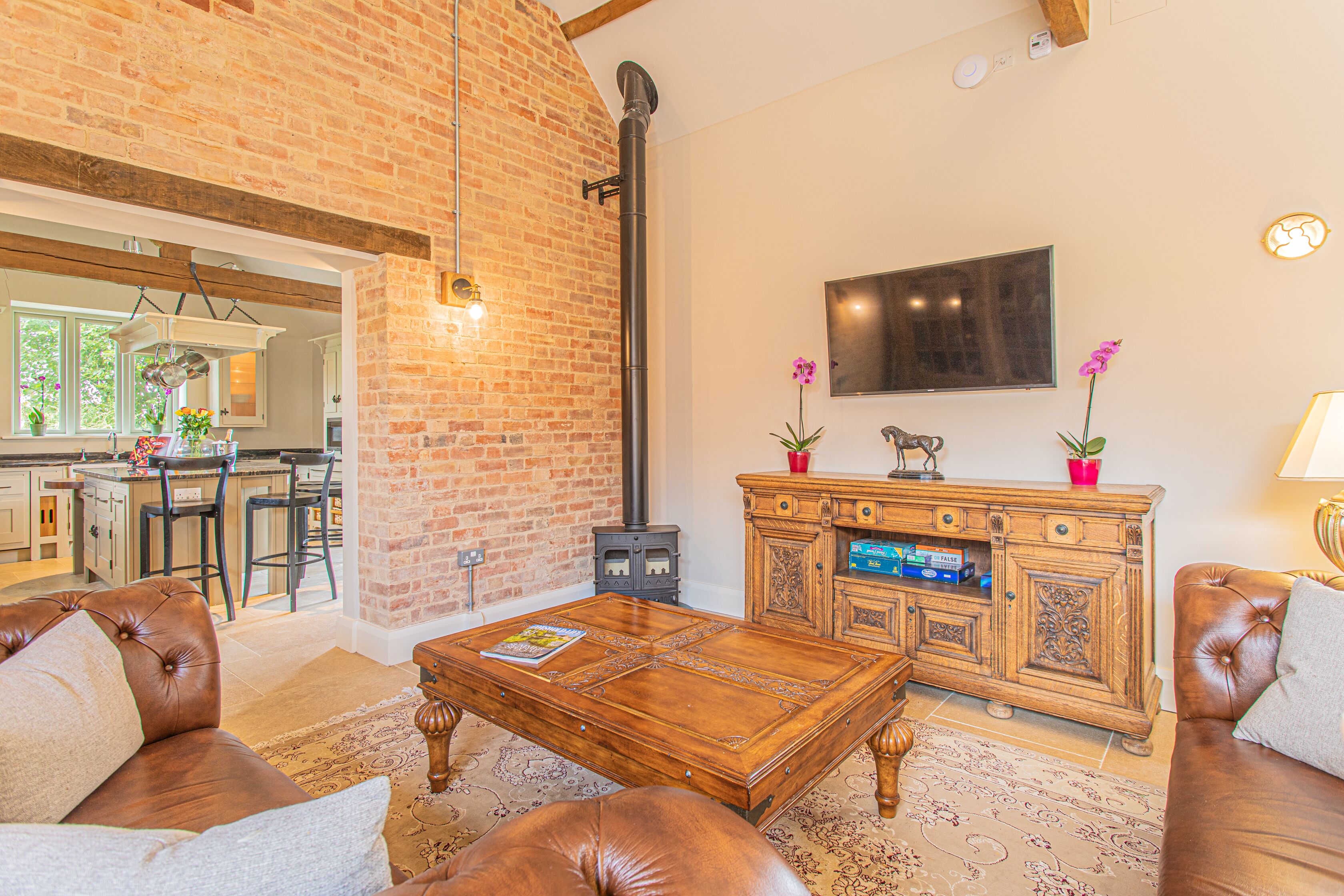 A living room with a brick wall, a wooden coffee table, leather sofas, a wooden cabinet, and a TV mounted on the wall.