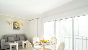 Une pièce lumineuse comprenant un canapé, une table à manger, des chaises et un balcon avec une balustrade.