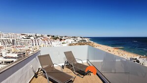 A balcony with two sun loungers overlooking a beach and a cityscape.