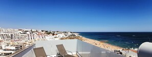 Un balcon avec deux chaises longues donnant sur une plage et offrant une vue sur la ville.