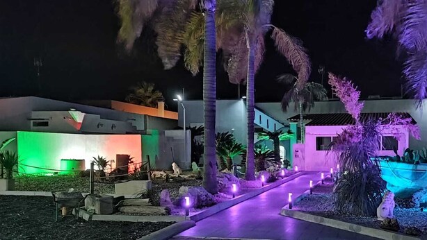 A nighttime view of a hotel with illuminated pathways and tropical landscaping.