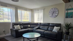 A modern living room with a black leather sectional sofa, a round coffee table, and a large wall clock. - LAKEVIEW Hot Tub Retreat Near Wineries! (Silver Creek)