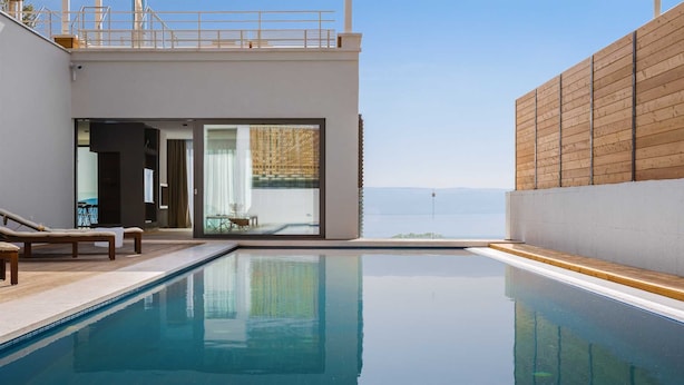 A modern pool area with a clear view of the sea, a lounge with a glass door, and a wooden wall.