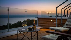 A balcony with a view of the sea, a bottle of champagne, two glasses, and a bowl of chocolates.
