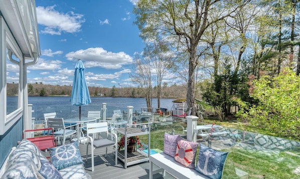 A deck with outdoor furniture, a blue umbrella, and a view of a lake.