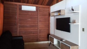 A modern living room with a wooden ceiling, a flat-screen TV mounted on a white wall, a wooden cabinet below, and a sliding wooden door. - Heated pool **FREE** + Air conditioning + 300MB Vivo fiber internet, Riviera Beach (Bertioga)