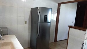 A compact kitchen with a stainless steel refrigerator, a sink, and a wooden cabinet. - Heated pool **FREE** + Air conditioning + 300MB Vivo fiber internet, Riviera Beach (Bertioga)