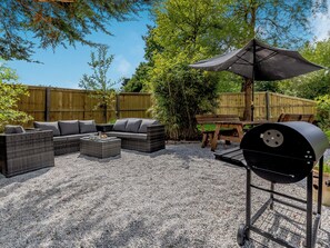 An outdoor patio with a wicker sofa, a table with drinks, a grill, and a wooden fence.