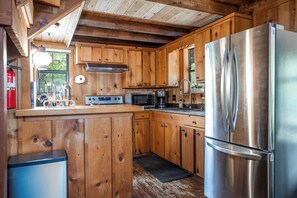 A kitchen with wooden cabinets, stainless steel appliances, and a built-in microwave. - Old Fellows Farmhouse | 2BR with Country Views (Kerrville)