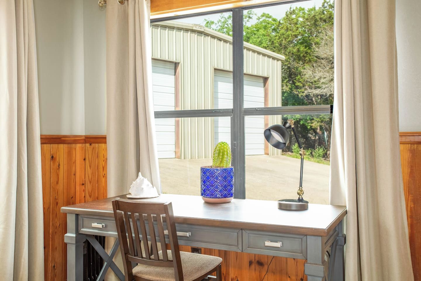 A desk with a chair, a cactus, a lamp, and a window with curtains.