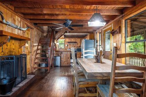 A wooden cabin interior with a dining area, kitchen, and a staircase. - Old Fellows Farmhouse | 2BR with Country Views (Kerrville)