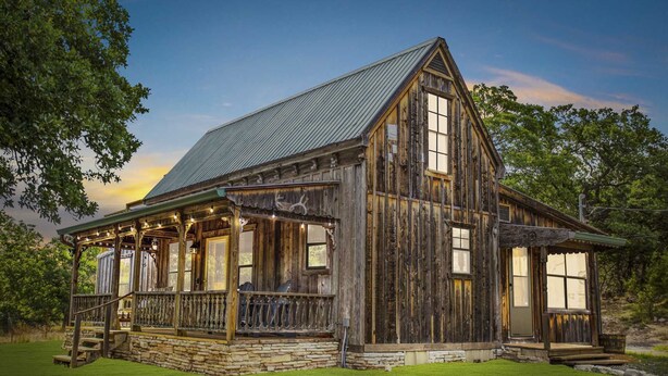 A rustic wooden cabin with a porch, stone foundation, and a metal roof. - Old Fellow's Farmhouse (Kerrville)