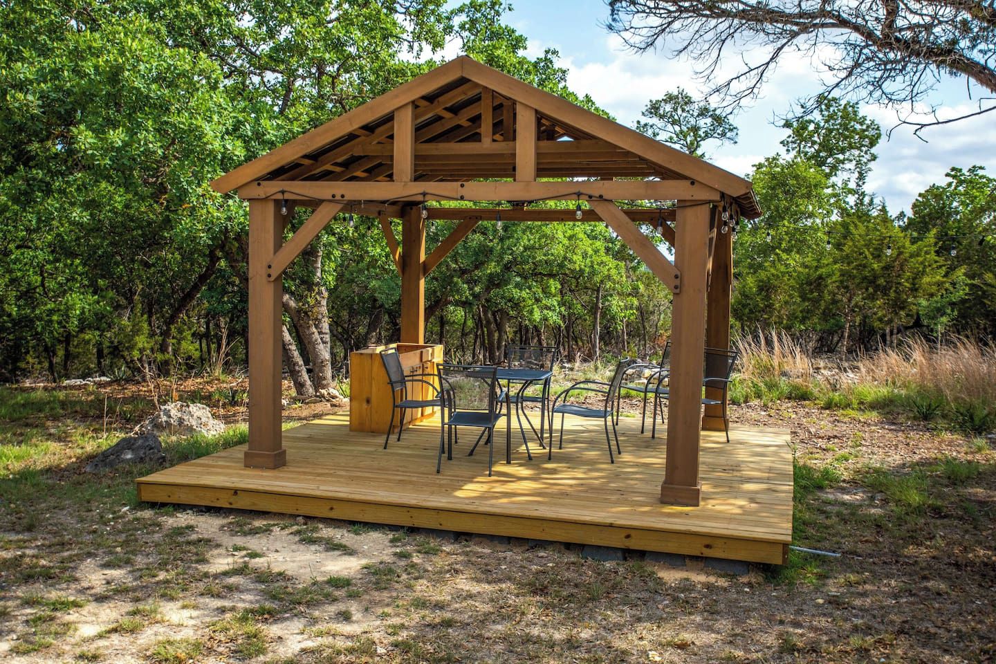Un quiosco de madera con una mesa y sillas, rodeado de árboles.