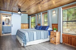 A bedroom with a bed, a nightstand, a dresser, and a window with curtains. - Old Fellows Farmhouse | 2BR with Country Views (Kerrville)