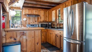 A rustic cabin kitchen with wooden cabinets, a stainless steel refrigerator, a microwave, and a gas stove. - Old Fellow's Farmhouse (Kerrville)