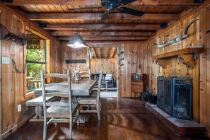 A rustic wooden cabin interior with a dining table, chairs, a ceiling fan, and a fireplace. - Old Fellows Farmhouse | 2BR with Country Views (Kerrville)
